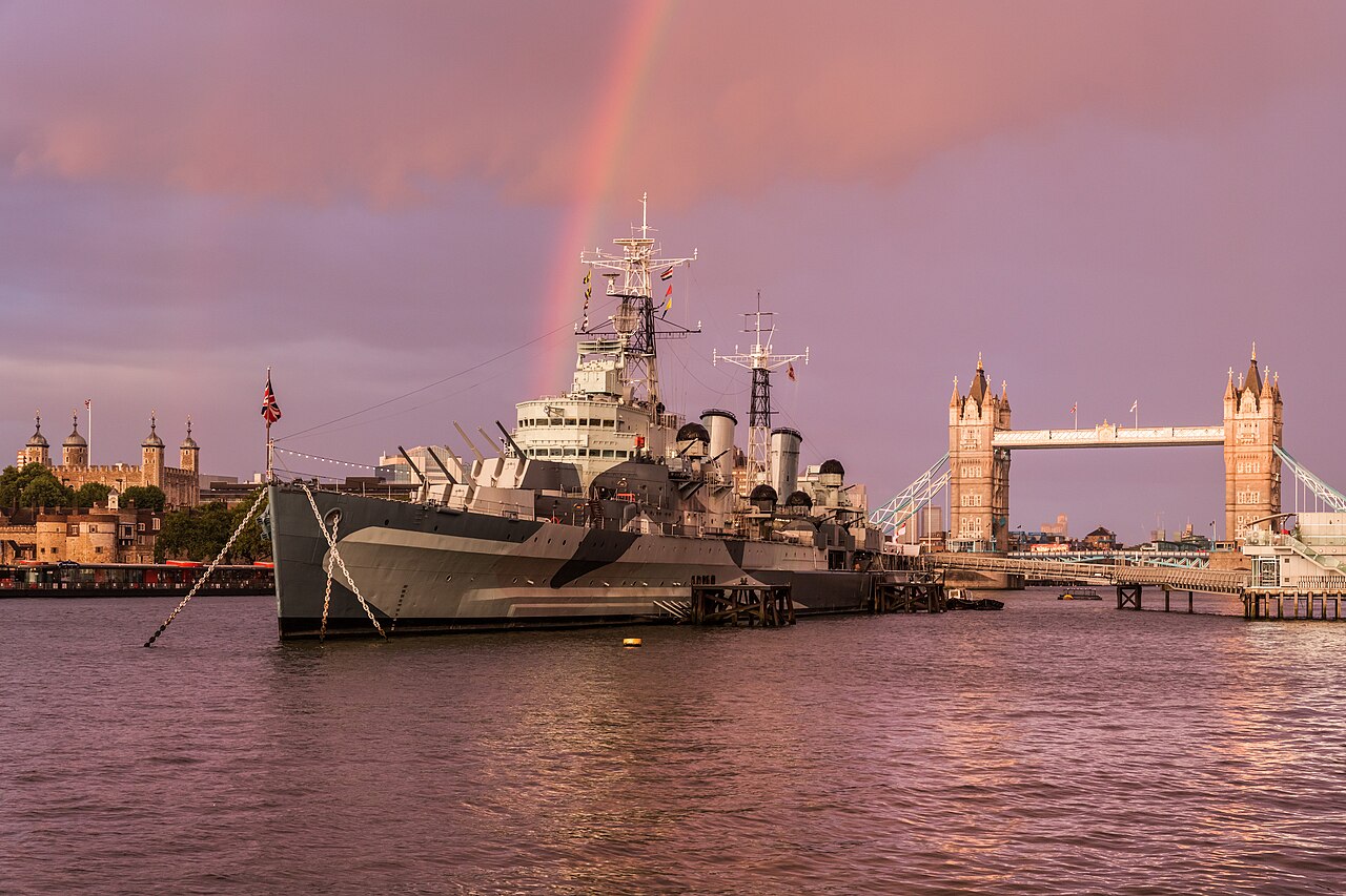HMS Belfast moored on the Thames near Tower Bridge under a rainbow