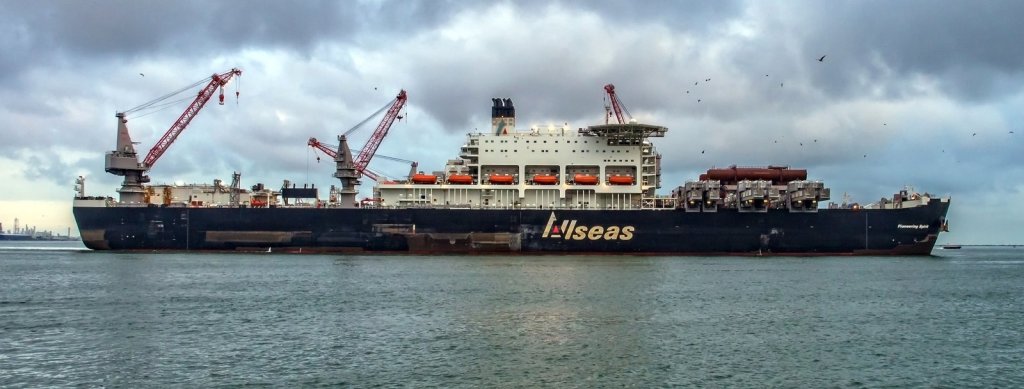 Broadside view of Pioneering Spirit at Rotterdam, with lifting beams along the forward deck and cranes aft.